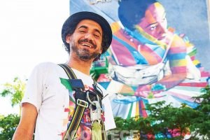 Imagem do artista Eduardo Kobra na vanguarda, com o mural na Torre do Carnaval ao fundo